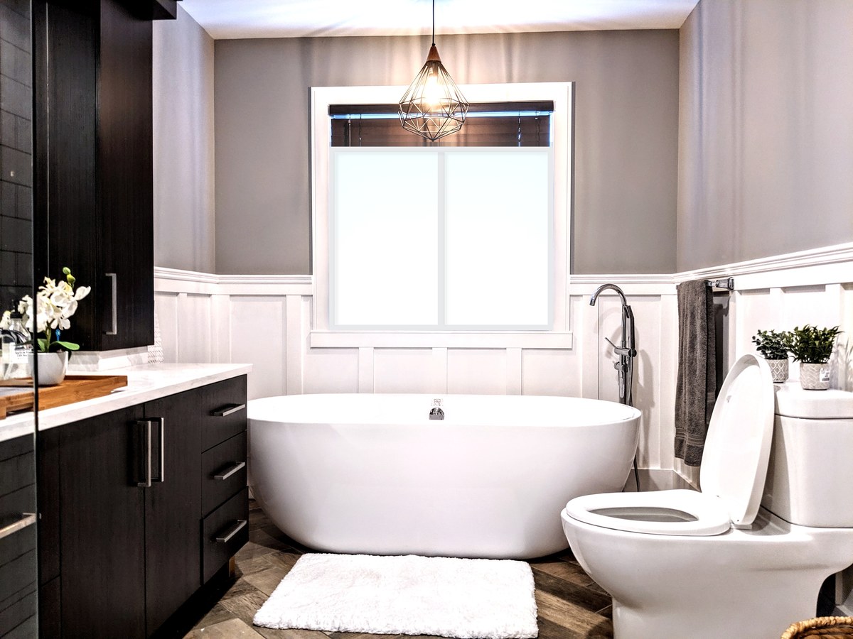 Renovated bathroom with a freestanding tub under a daylit window, board-and-batten wainscoting and a dark wood vanity